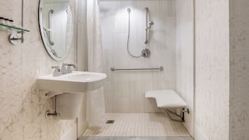 A modern bathroom with a sink, mirror, shower, and a small bench.