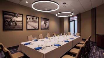 Un salón de conferencias con una larga mesa dispuesta para una reunión, fotografías enmarcadas en la pared y luminarias modernas.