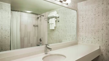 Un baño con un espejo grande, un lavamanos y una zona de ducha.