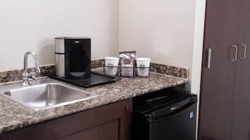 A kitchen with a stainless steel sink, a coffee maker, and a coffee dispenser.