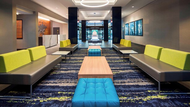 Un hall de hotel con una zona de estar central, un mostrador de recepción y vistas al exterior.