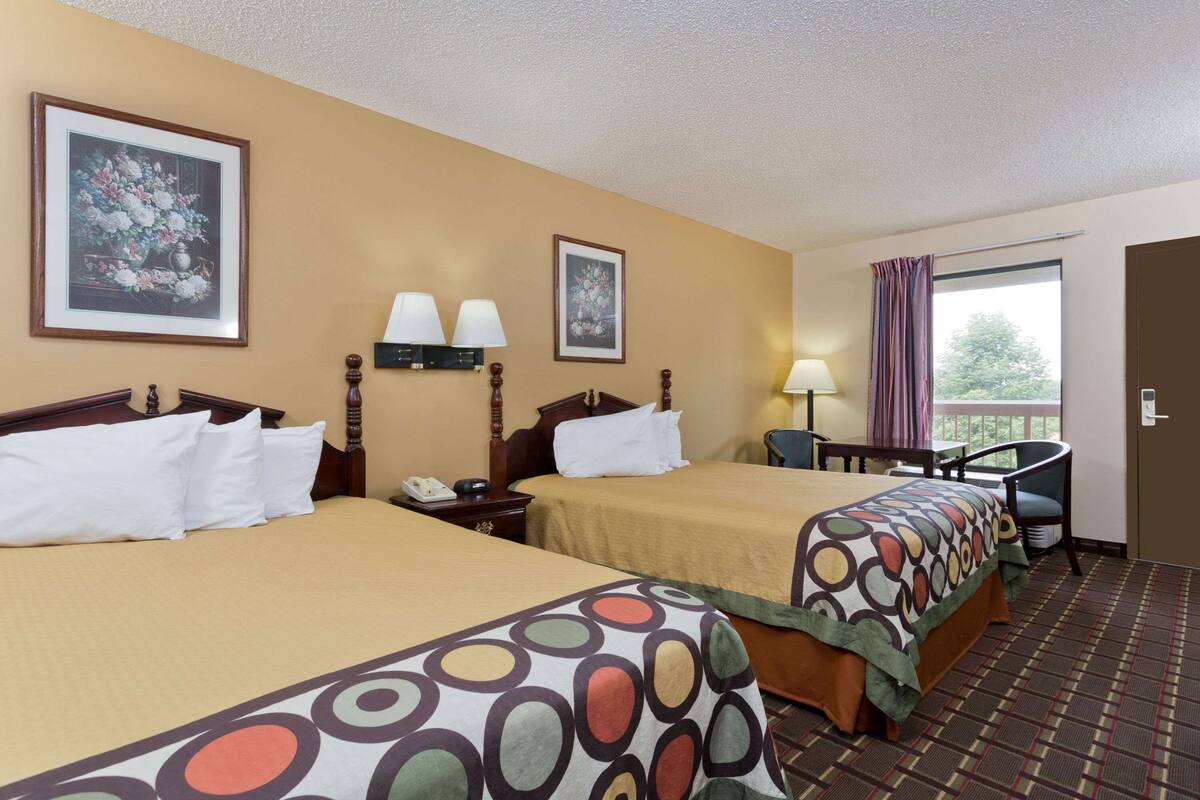 A hotel room with two beds, a desk, a chair, and a window with curtains.