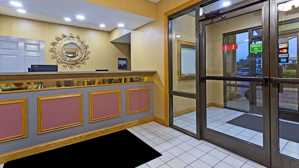 Zona de recepción con mostrador de check-in, un espejo grande y puerta de vidrio que da al exterior.