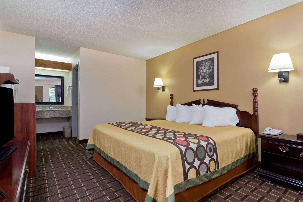 A hotel room with a bed, bedside table, lamp, and a bathroom with a mirror and sink.