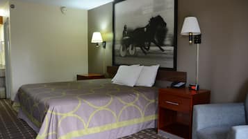 Habitación de hotel con una cama grande, una mesita de noche con lámpara, una silla e imagen enmarcadas en la pared.