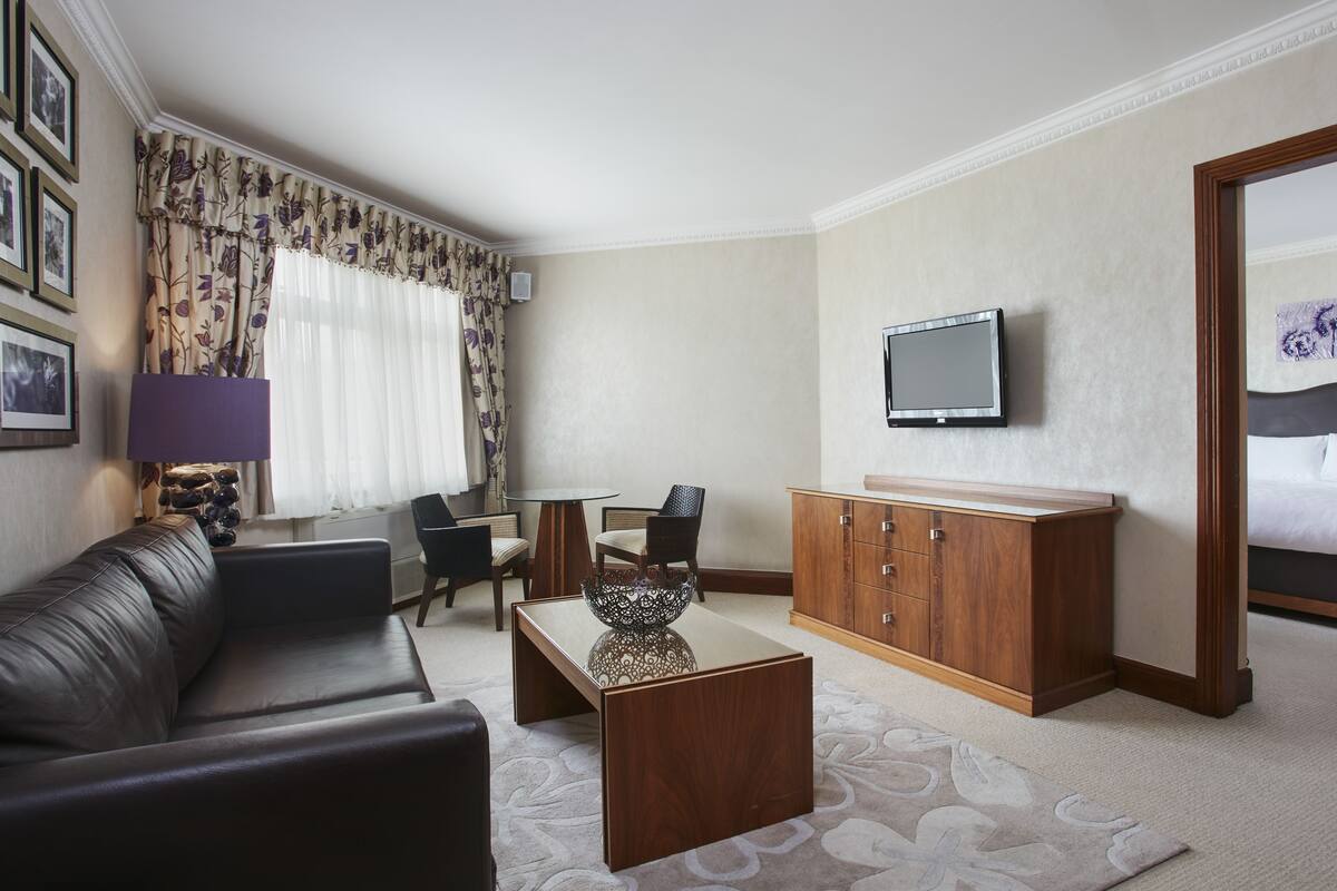 A hotel room with a sofa, a wooden cabinet, a television, a bed, and a patterned rug.
