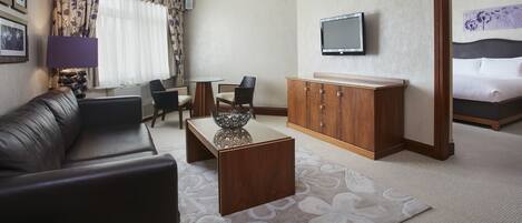 A hotel room with a sofa, a wooden cabinet, a television, a bed, and a patterned rug.