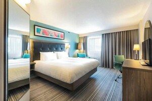 Habitación de hotel con una cama grande, un escritorio, una silla, un espejo y un cuadro en la pared.