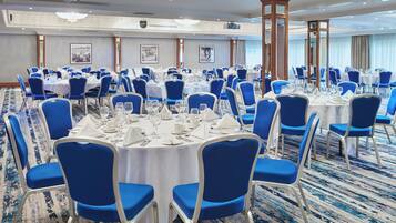 A conference room with round tables, blue chairs, and white tablecloths.