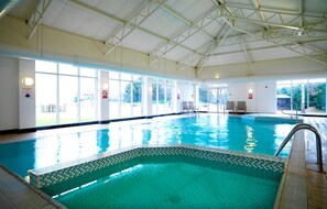 An indoor swimming pool with clear glass walls, a tiled edge, and a metal handrail.