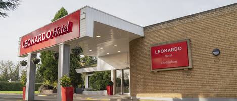 The exterior of the Leonard Hotel in Cheltenham, featuring a prominent red sign, a covered entrance, and potted plants.