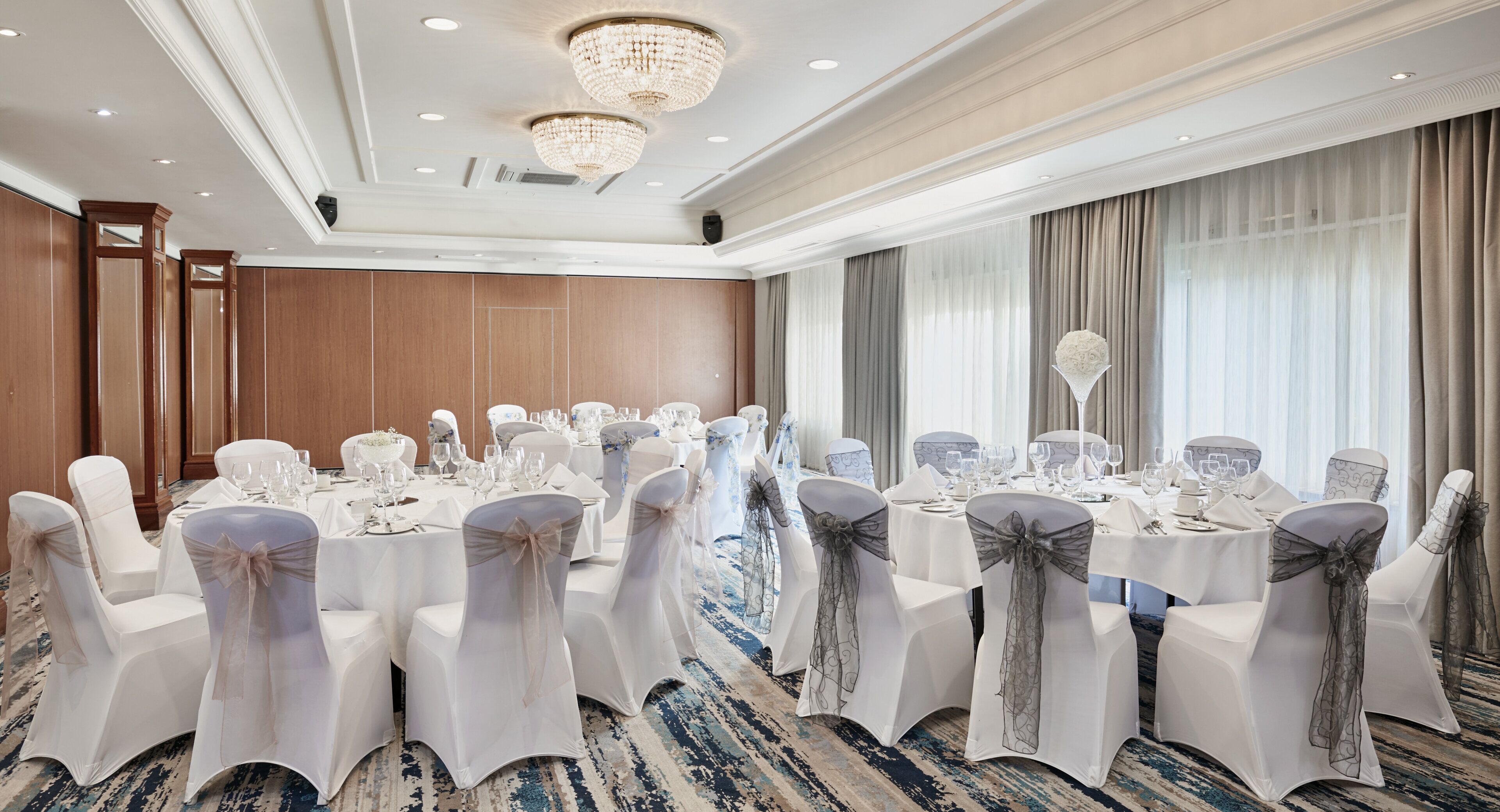 A banquet hall with round tables, white chairs, and chandeliers.