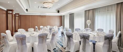 A banquet hall with round tables, white chairs, and chandeliers.