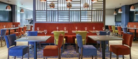 A restaurant with booths, tables, and chairs, featuring a patterned floor and pendant lighting.