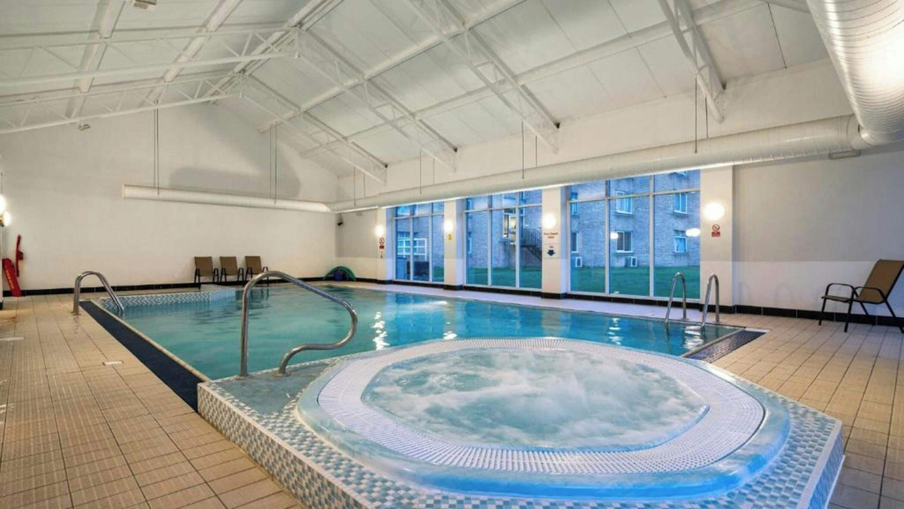 Une piscine intérieure avec un jacuzzi, un revêtement de sol carrelé et des fenêtres.