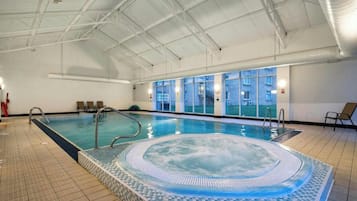 Une piscine intérieure avec un jacuzzi, un revêtement de sol carrelé et des fenêtres.