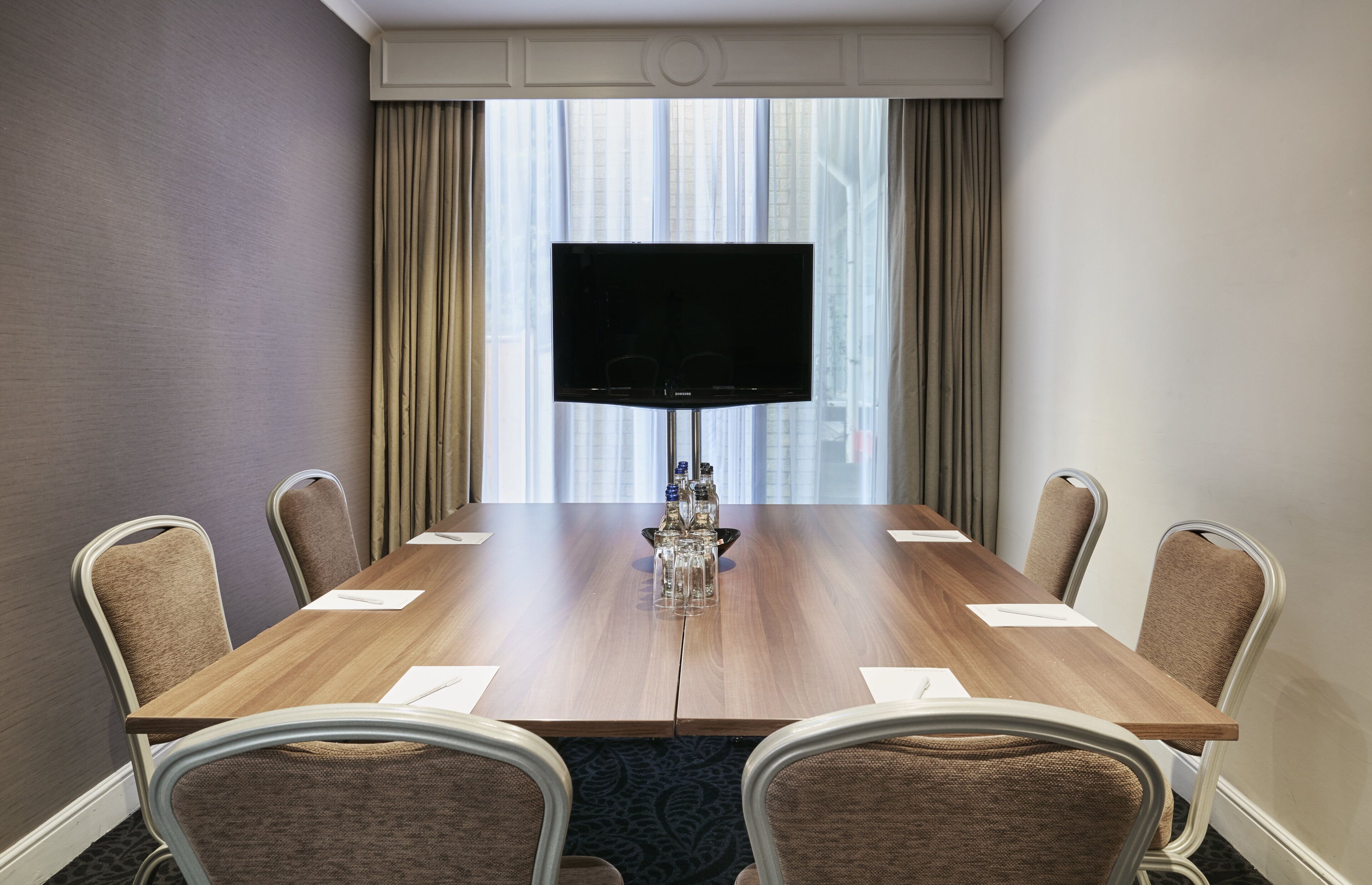 A conference room with a large flat-screen TV, a wooden table, and six chairs.