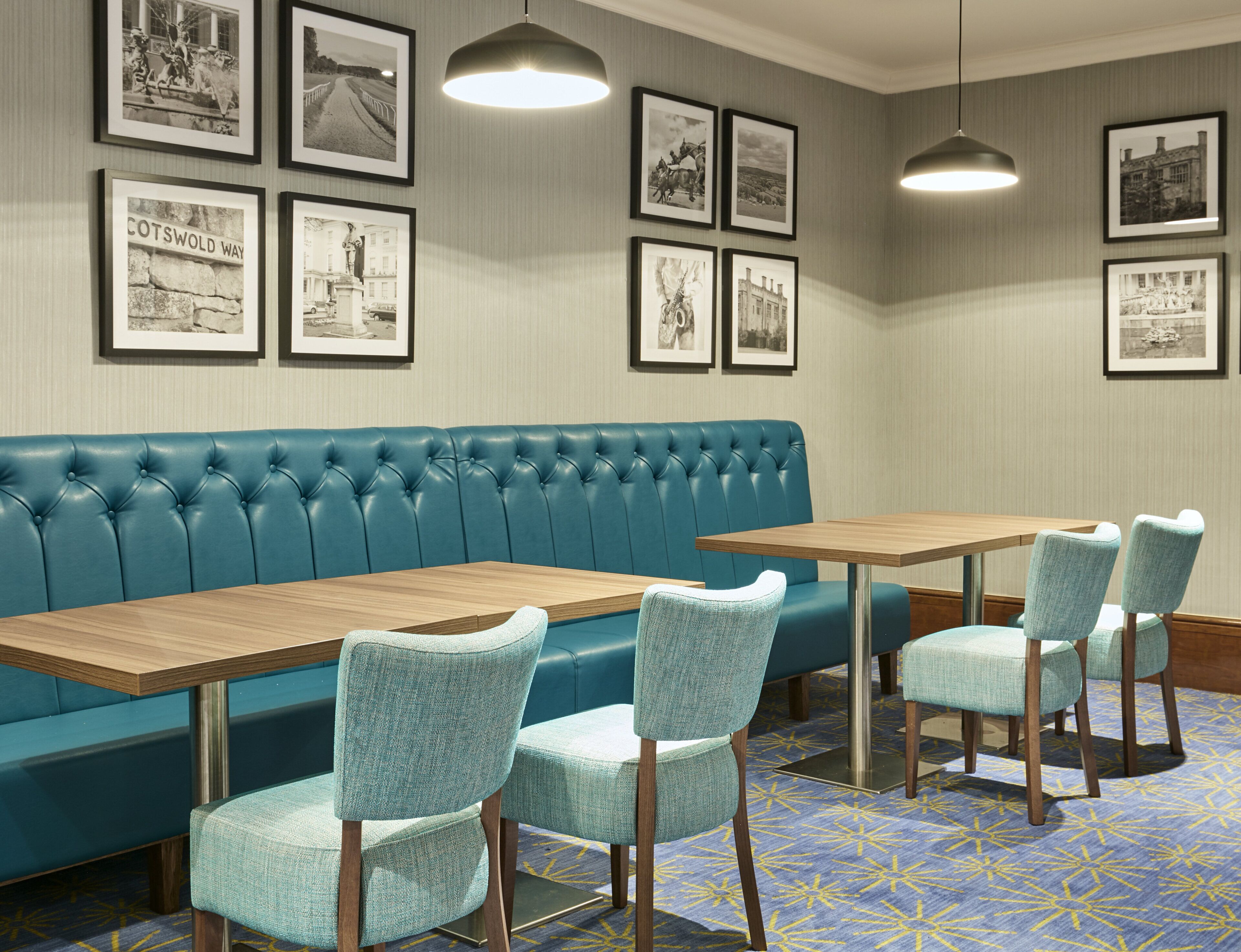 A room with a blue upholstered bench, wooden tables, and light blue chairs.