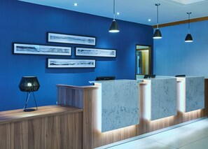 A reception desk with a wooden counter and marble panels, blue walls, and framed artwork.