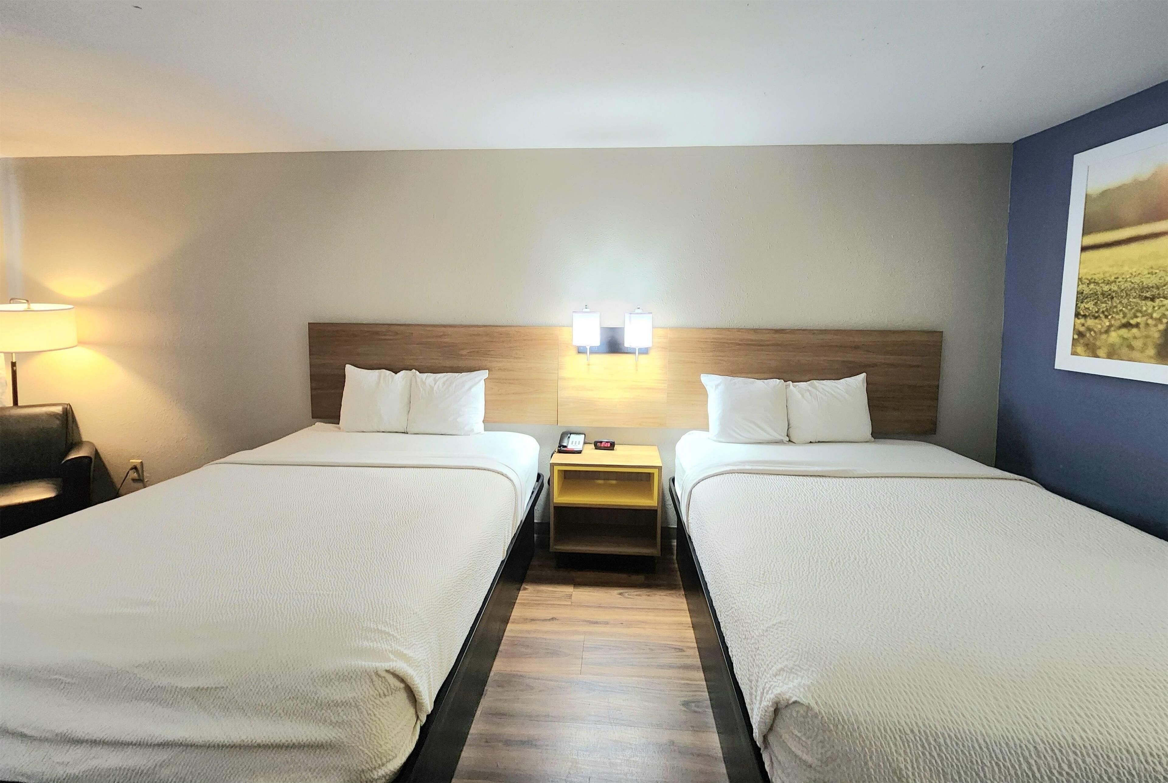 A hotel room with two beds, a nightstand with a lamp, and a wall-mounted light fixture.