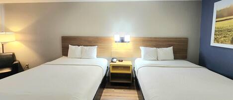 A hotel room with two beds, a nightstand with a lamp, and a wall-mounted light fixture.