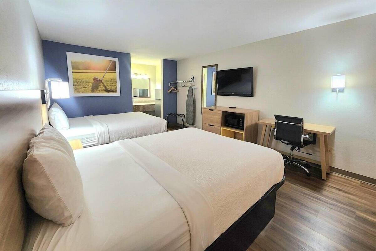 A hotel room with a large bed, a desk, a TV, and a painting on the wall.