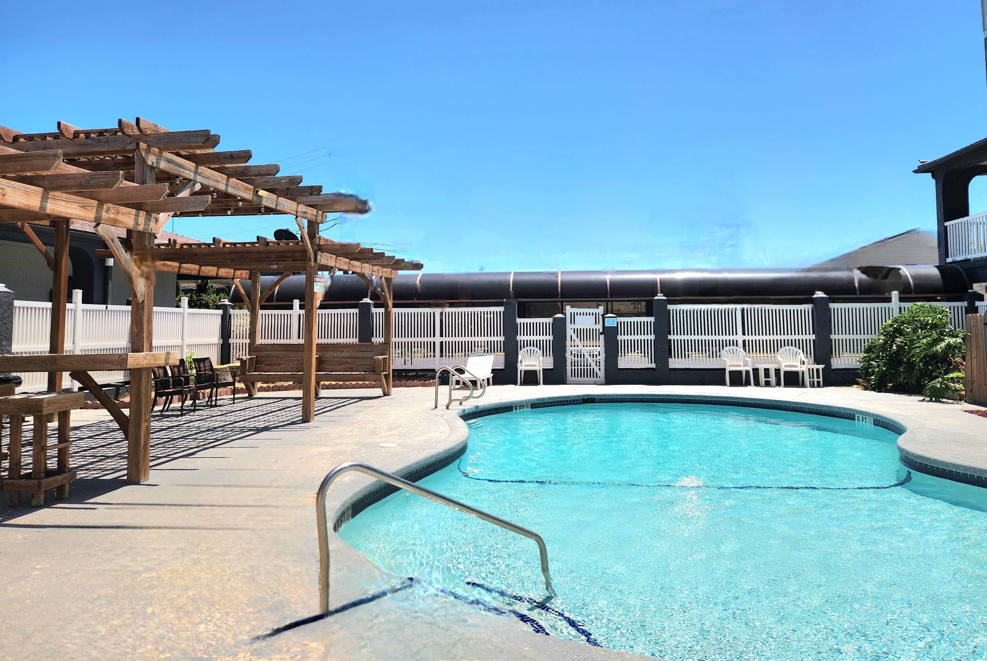 A pool area with a wooden pergola, lounge chairs, and a fenced deck.