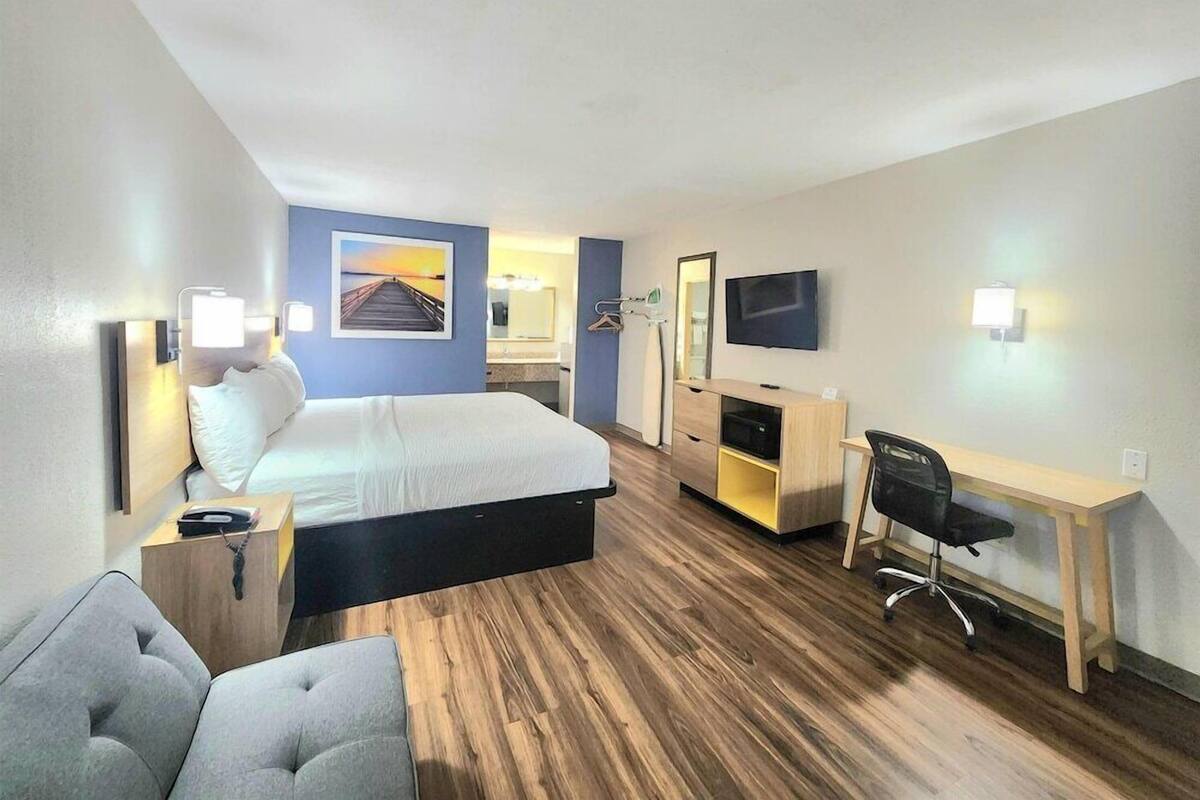 A hotel room with a bed, a desk, a chair, a TV, and a painting on the wall.