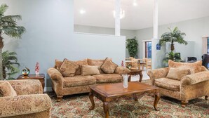 A spacious living room with patterned sofas, a wooden coffee table, and a decorative vase. - Days Inn by Wyndham Portland/Corpus Christi (Portland)