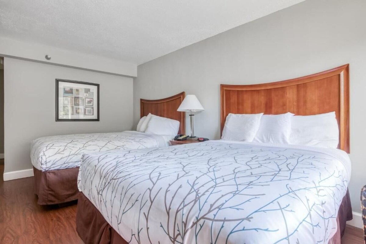A hotel room with two beds, a framed picture on the wall, and a nightstand with a lamp.