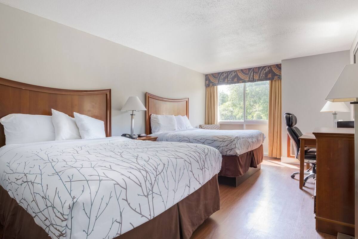 A hotel room with two beds, a desk, a chair, and a window with curtains.