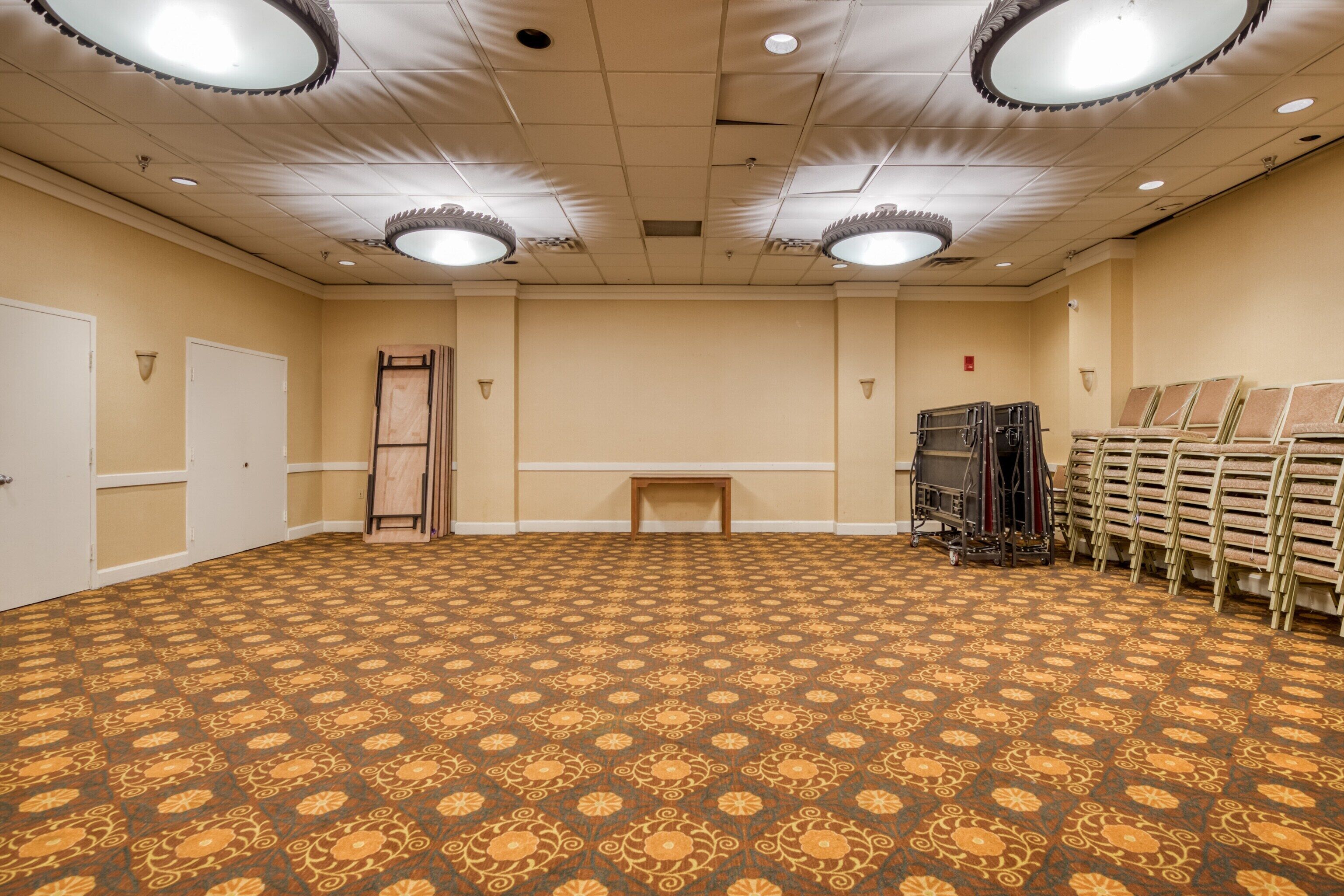 A large, carpeted room with a patterned floor, a wooden bench, and a stack of chairs.