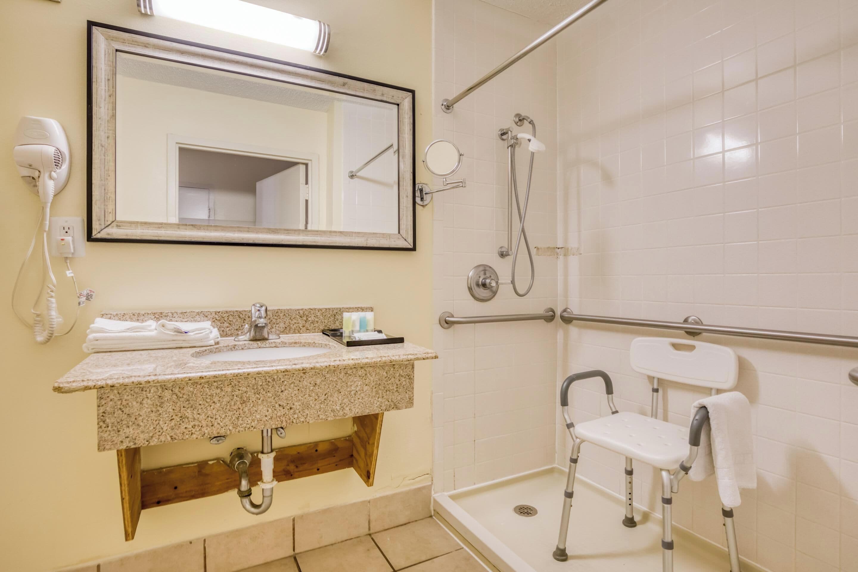 A bathroom with a sink, mirror, towel rack, and a wheelchair-accessible shower area.