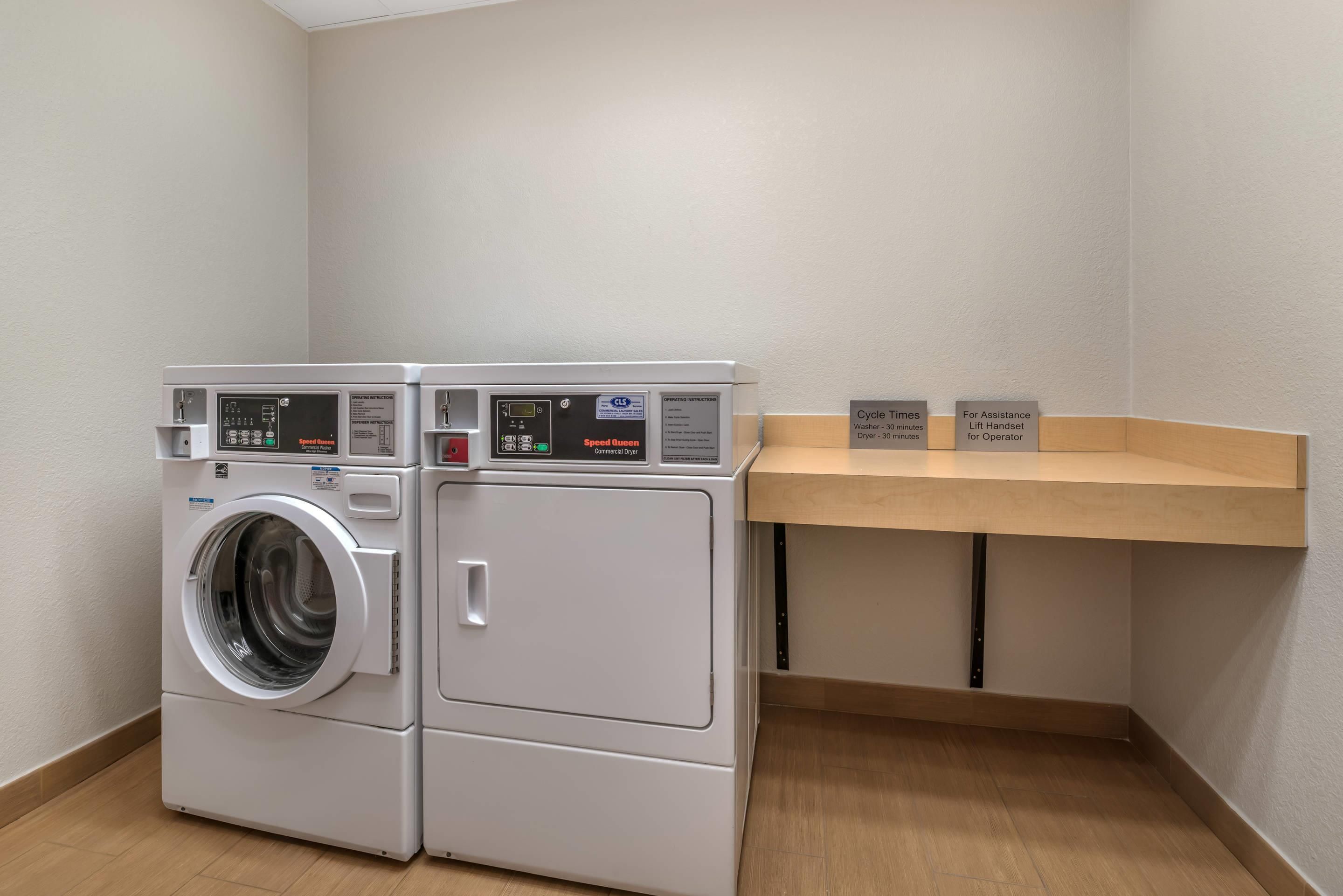 A laundry facility with a front-loading washer and dryer, operating instructions, and cycle times.