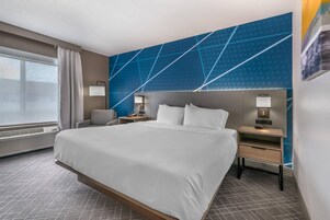 Habitación de hotel con una cama grande, dos mesitas de noche, una silla, una ventana con cortinas y un diseño geométrico azul en la pared.
