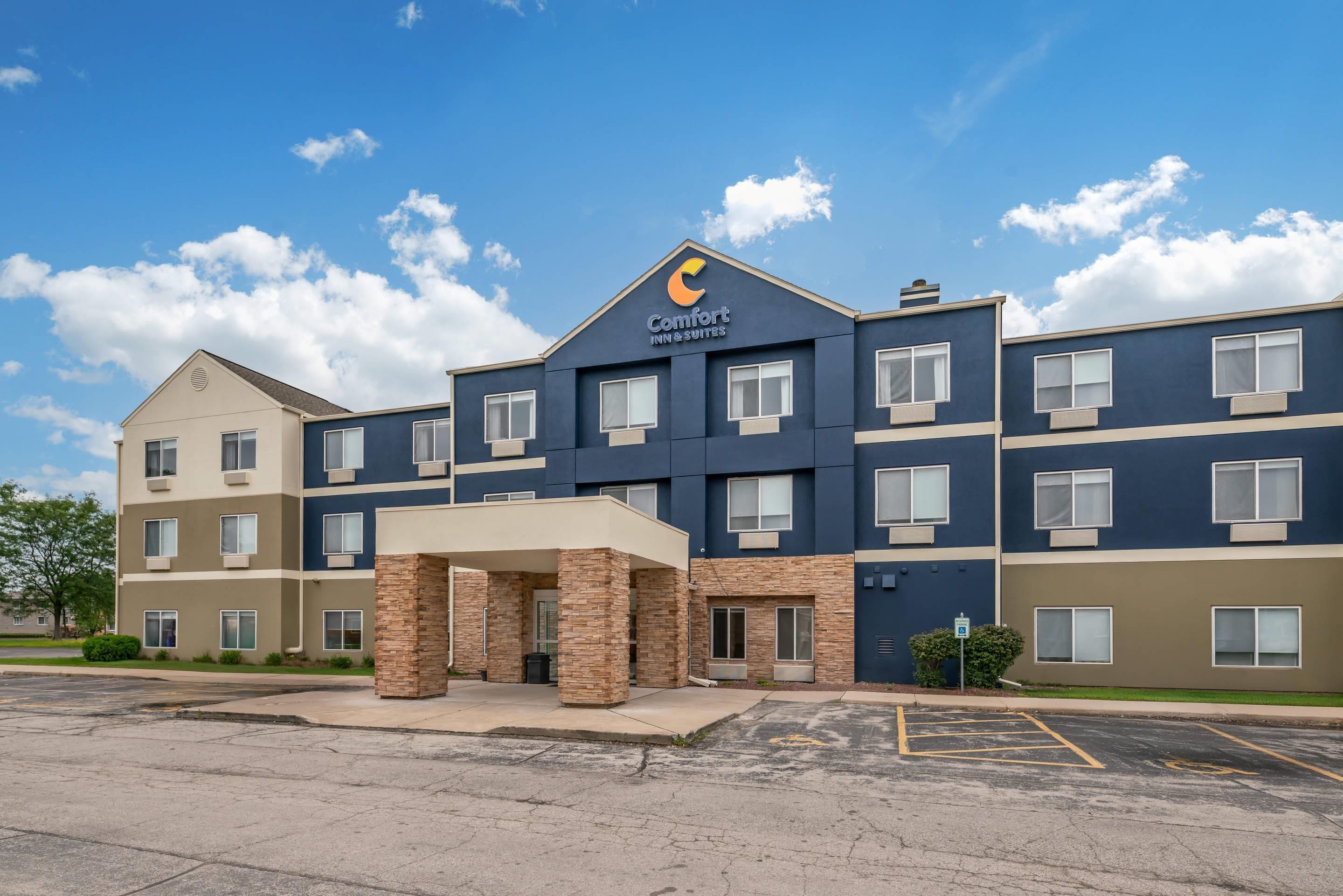 A multi-story hotel with a prominent Comfort Inns & Suites sign, a covered entrance, and a parking lot.