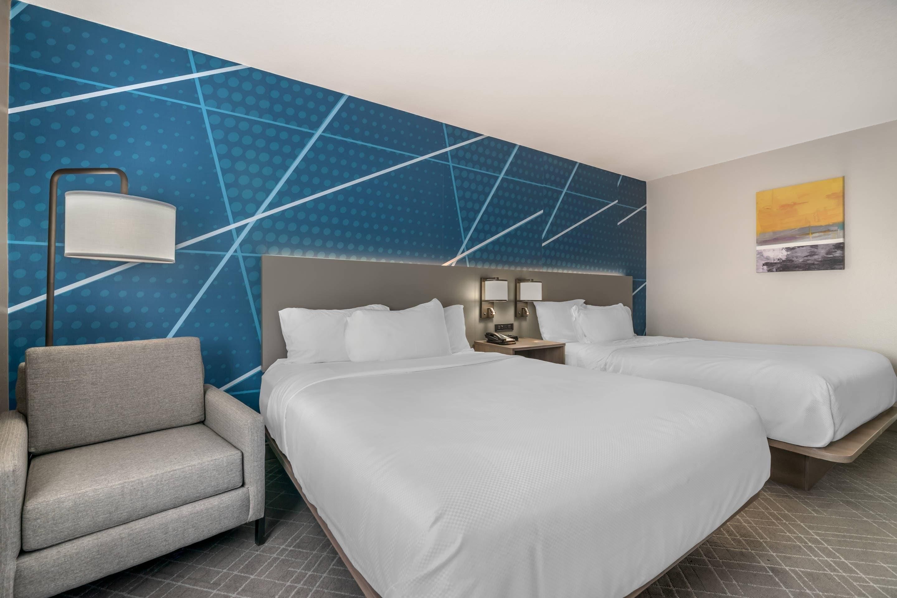 Ein Hotelzimmer mit zwei Betten, einem Sessel, einem Nachttisch mit Lampe und einer Wand mit geometrischem Muster.