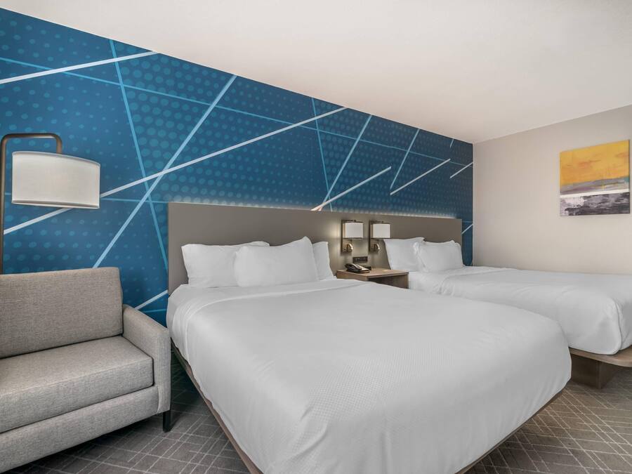 Ein Hotelzimmer mit zwei Betten, einem Sessel, einem Nachttisch mit Lampe und einer Wand mit geometrischem Muster.