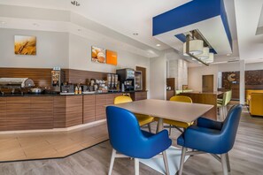 Een moderne keuken met een centraal eiland, koffiehoek en zithoek met blauwe stoelen.