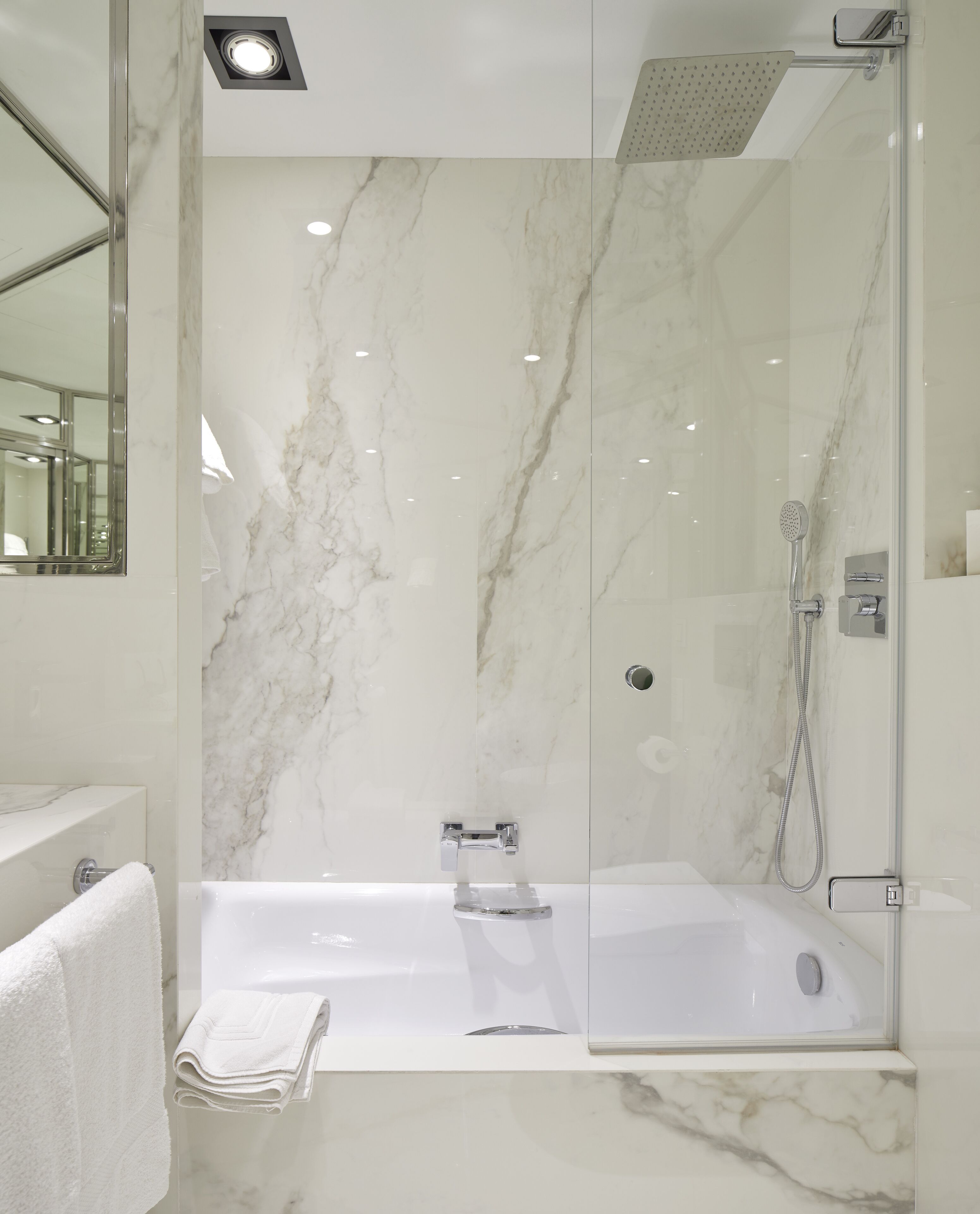 A modern bathroom with a glass-enclosed shower, a white marble wall, and a visible towel rack.