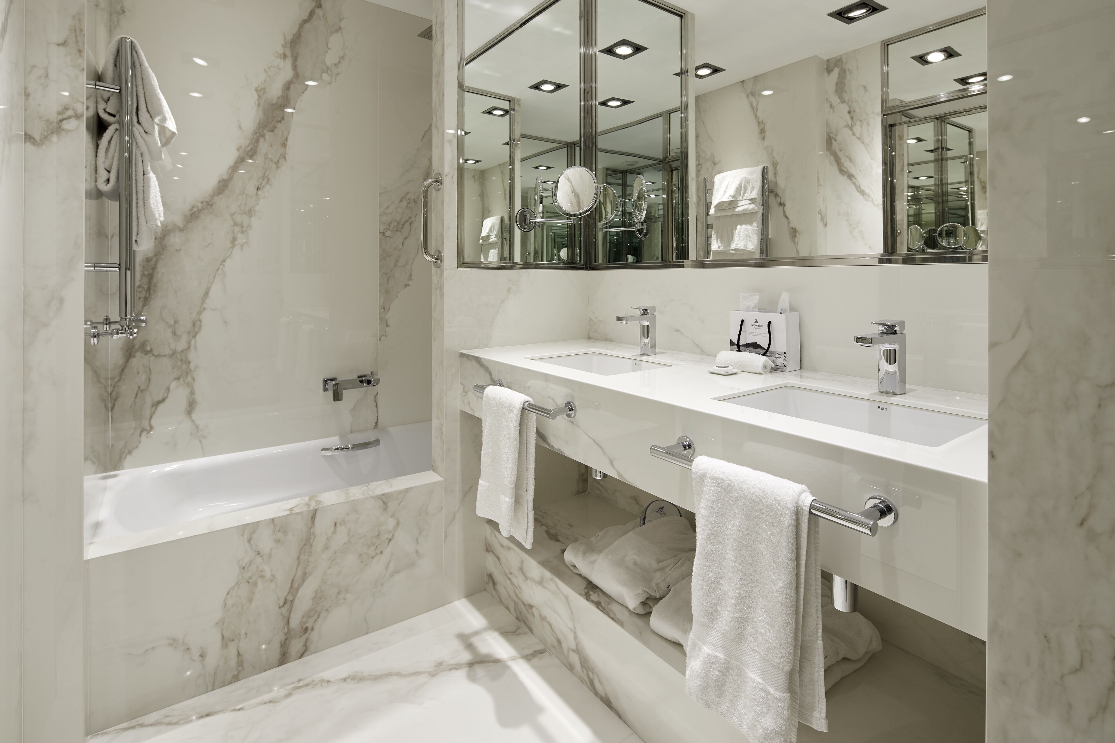 A modern bathroom with a marble floor, a bathtub, two sinks, and a large mirror.