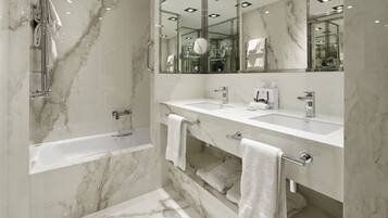 A modern bathroom with a marble floor, a bathtub, two sinks, and a large mirror.