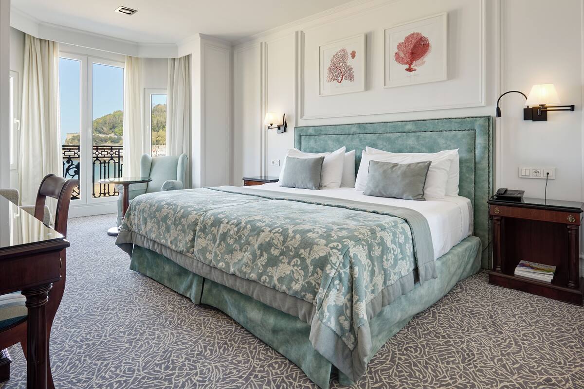 Een hotelkamer met een groot bed, een stoel, een tafel en uitzicht op het groen.