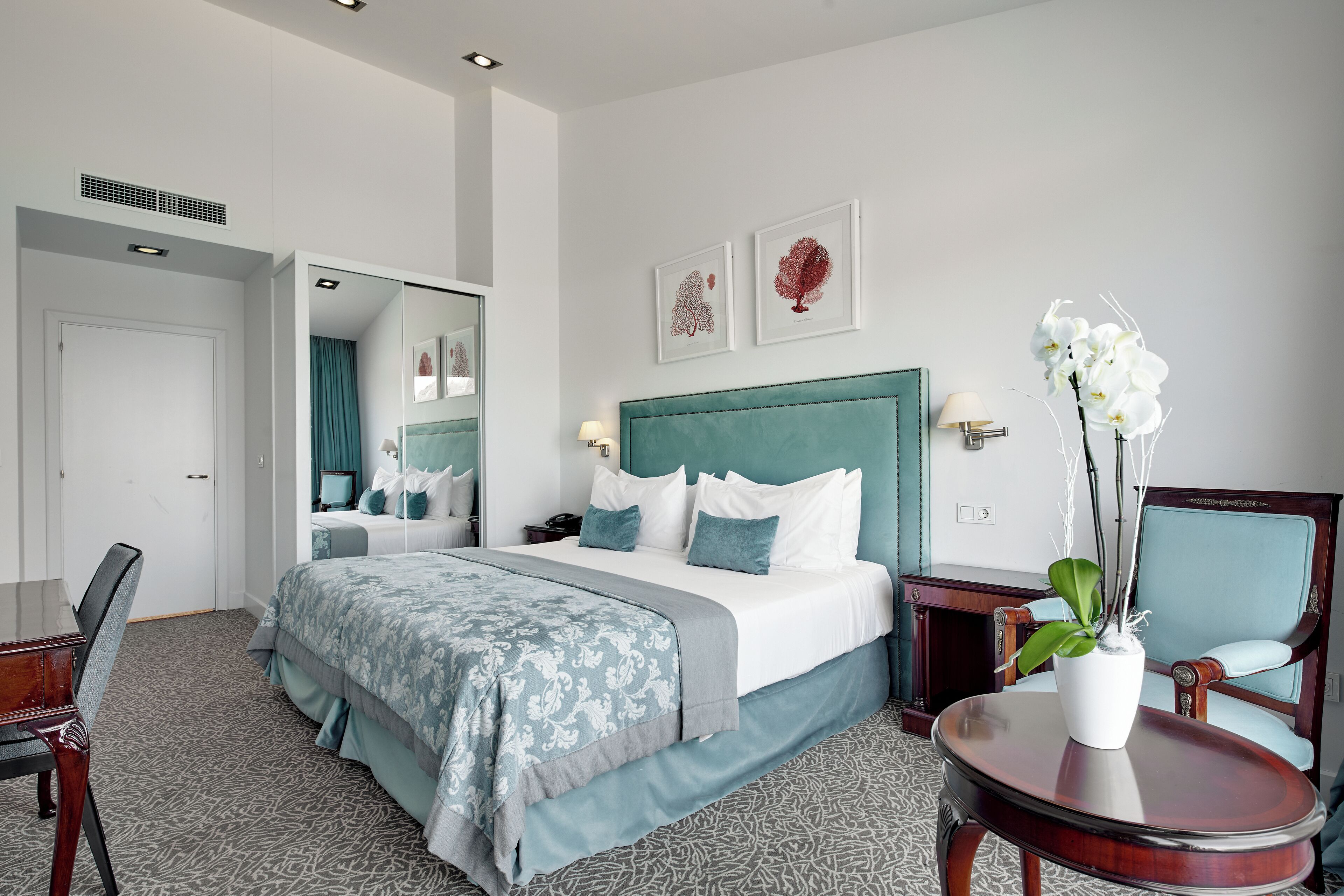 Une chambre d’hôtel avec un grand lit, un bureau, une chaise, une petite table et une plante en pot.