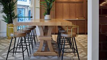 Un comedor moderno con una mesa de madera y taburetes de bar, rodeado de plantas en macetas y un suelo con diseño.