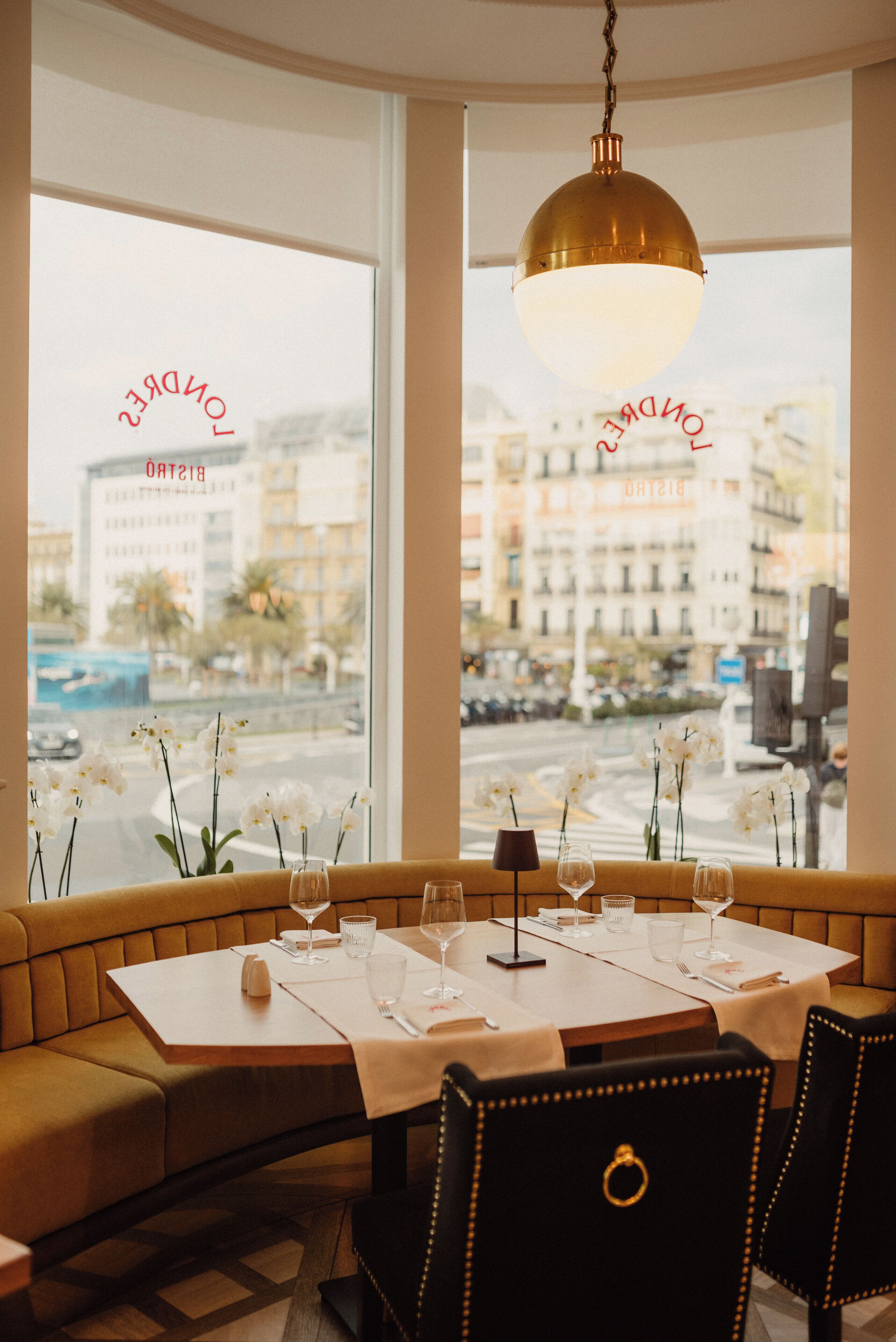 A restaurant with a table set for two, a sofa, and a view of the city through large windows.