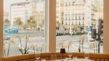 A restaurant with a table set for two, a sofa, and a view of the city through large windows.