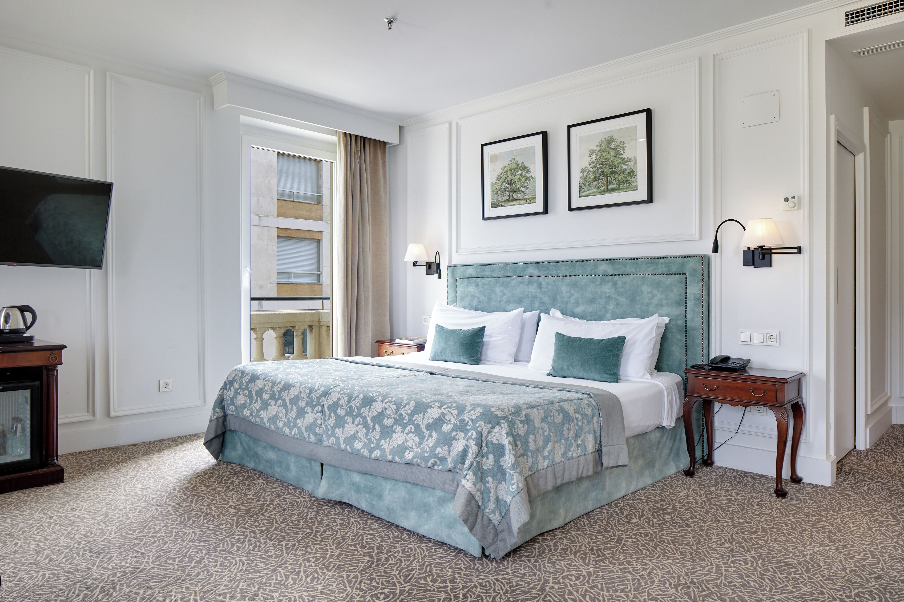 A neatly arranged bedroom with a large bed, a bedside table, and a nightstand. There are two framed pictures on the wall above the bed.