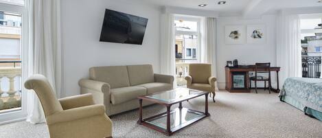 A living room with a sofa, armchairs, a glass coffee table, and a TV mounted on the wall.
