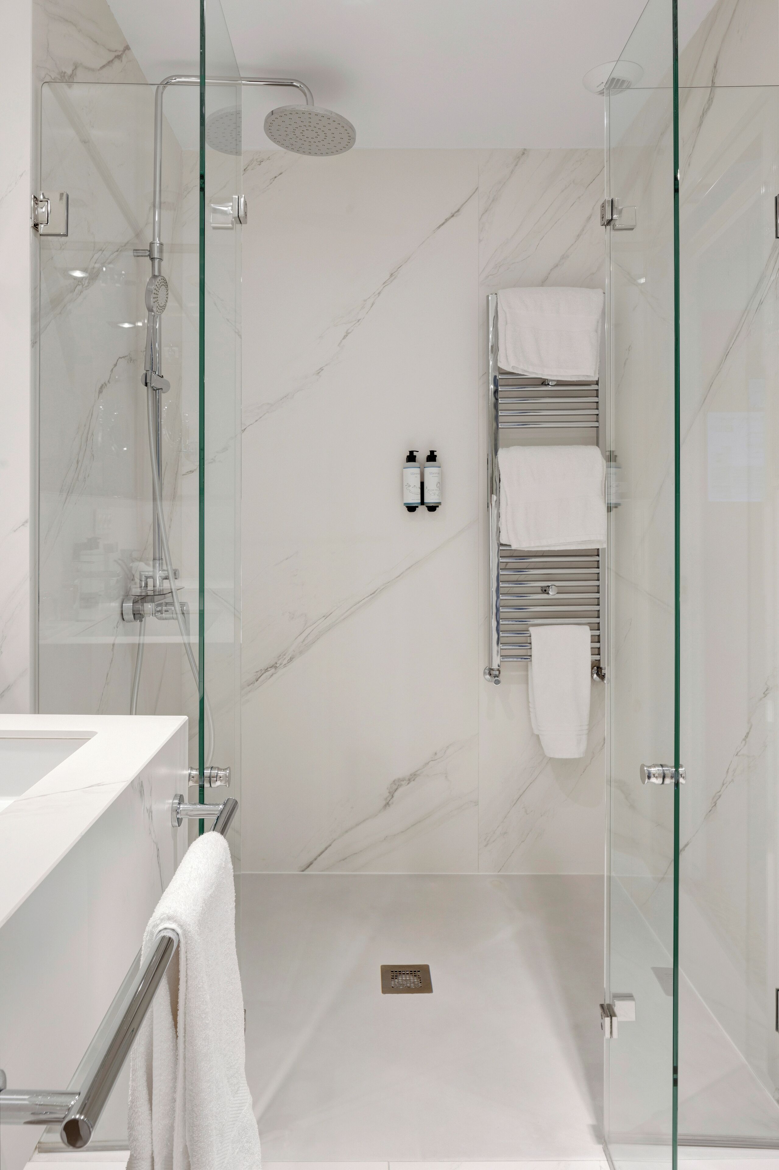 A modern bathroom with a glass-enclosed shower, marble walls, and a white sink.